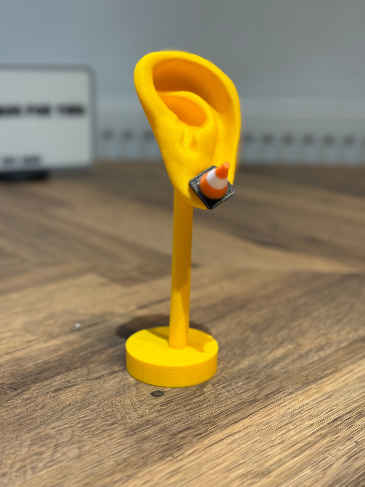 Yellow ear-shaped stand with a small cone earring by Not Made For This on a wooden surface