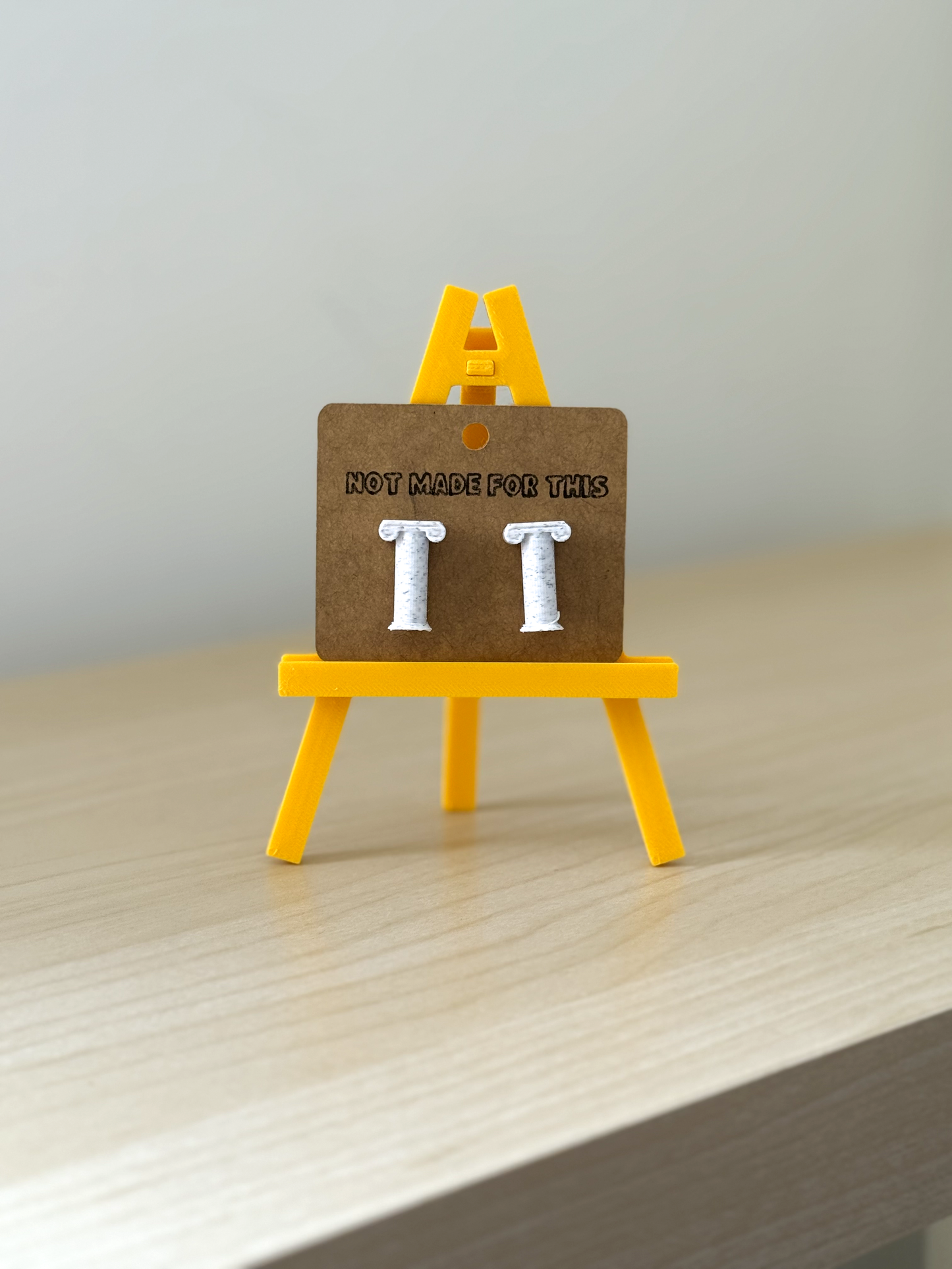 Earring card with 'Not Made For This' text and pillar earrings on a yellow stand.