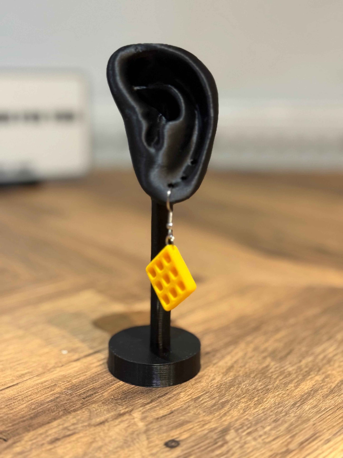 Yellow Not Made For This waffle-shaped earring on a black ear stand with a blurred background