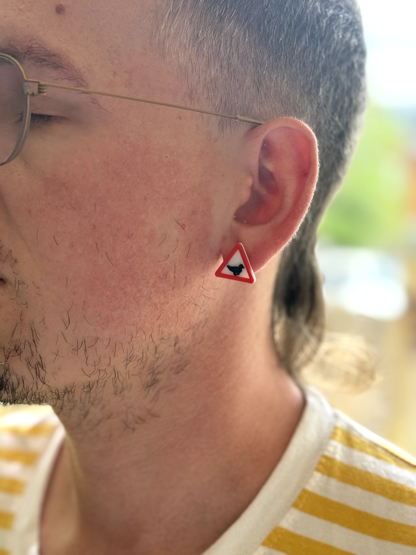 Person wearing a red triangle earring with a black symbol, close-up of ear and neck.