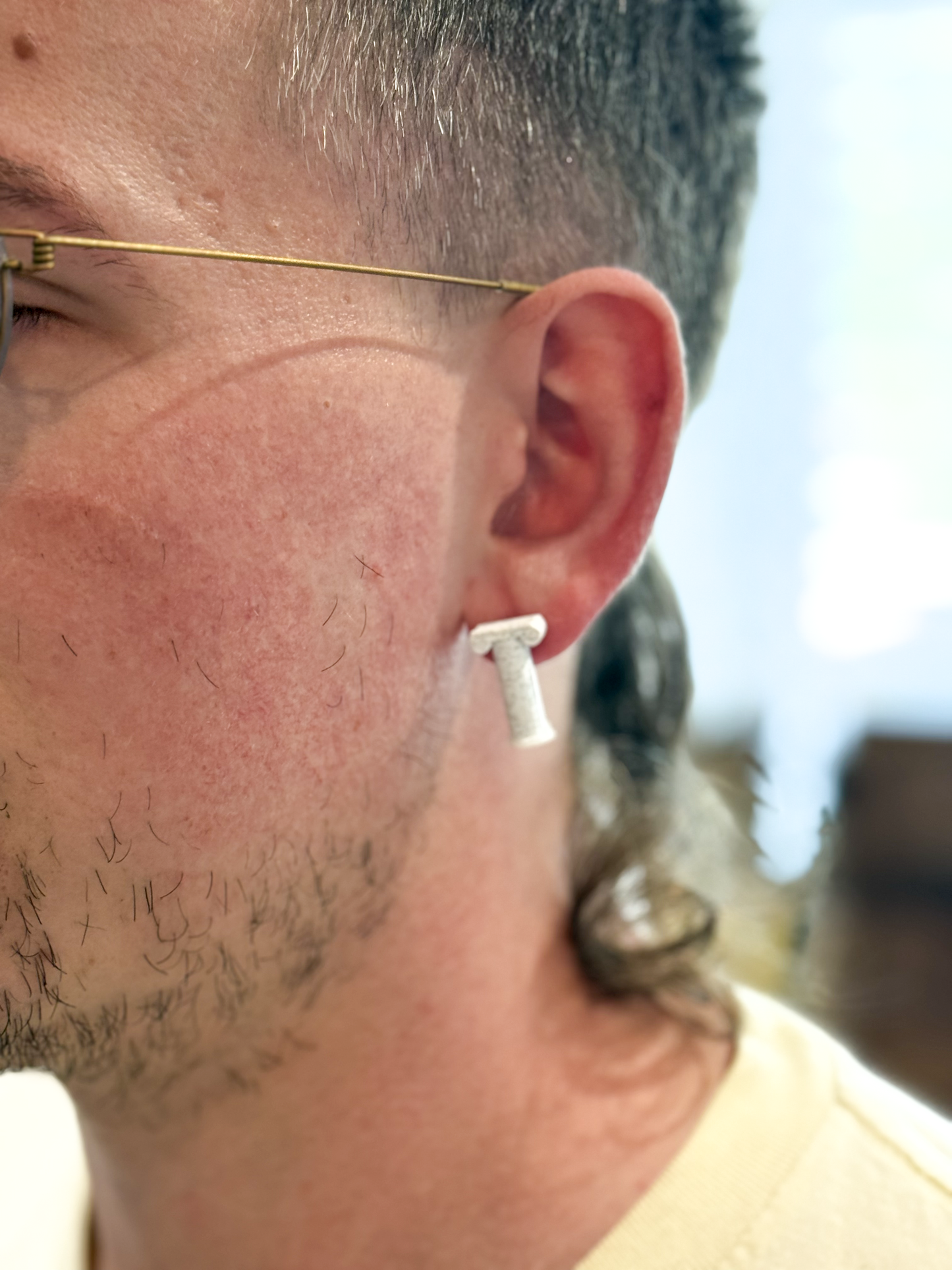 Close-up of a person wearing a white Not Made For This pillar earring with a blurred background