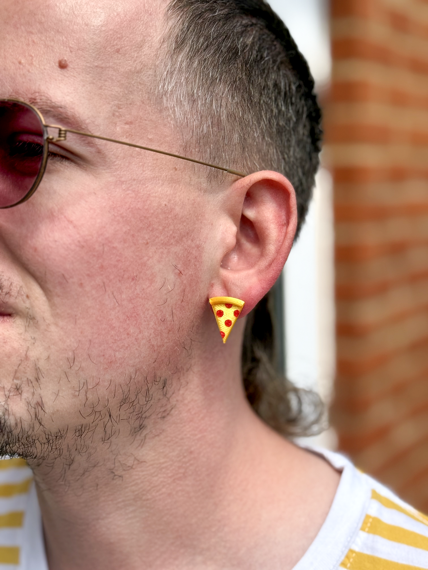 Person wearing a Not Made For This pizza-shaped earring with a blurred background