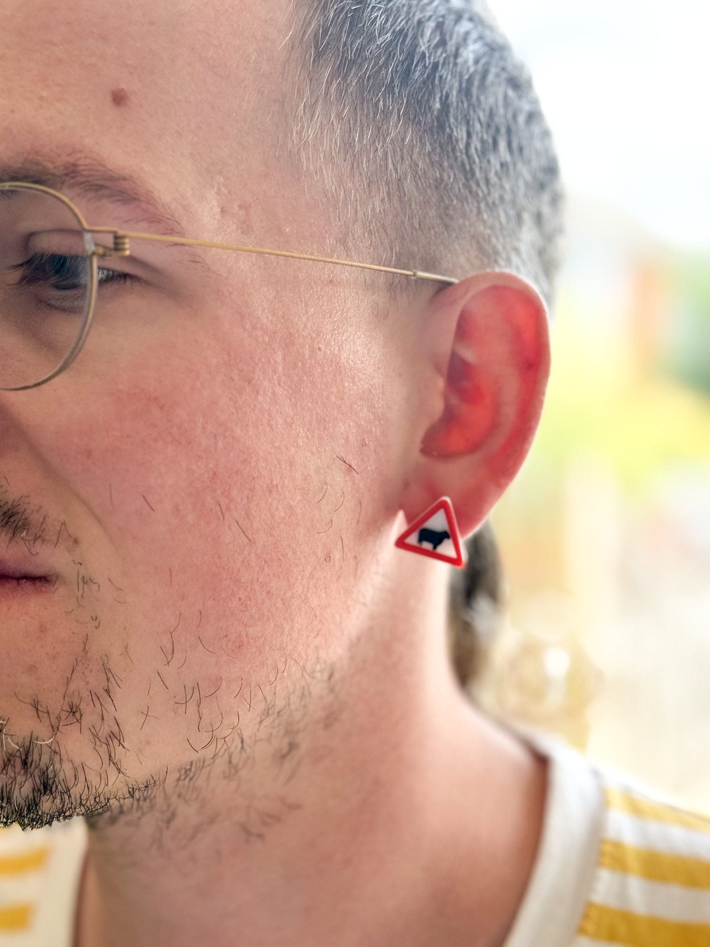 Close-up of a person wearing glasses with a Not Made For This small red triangle earring featuring a cow design.