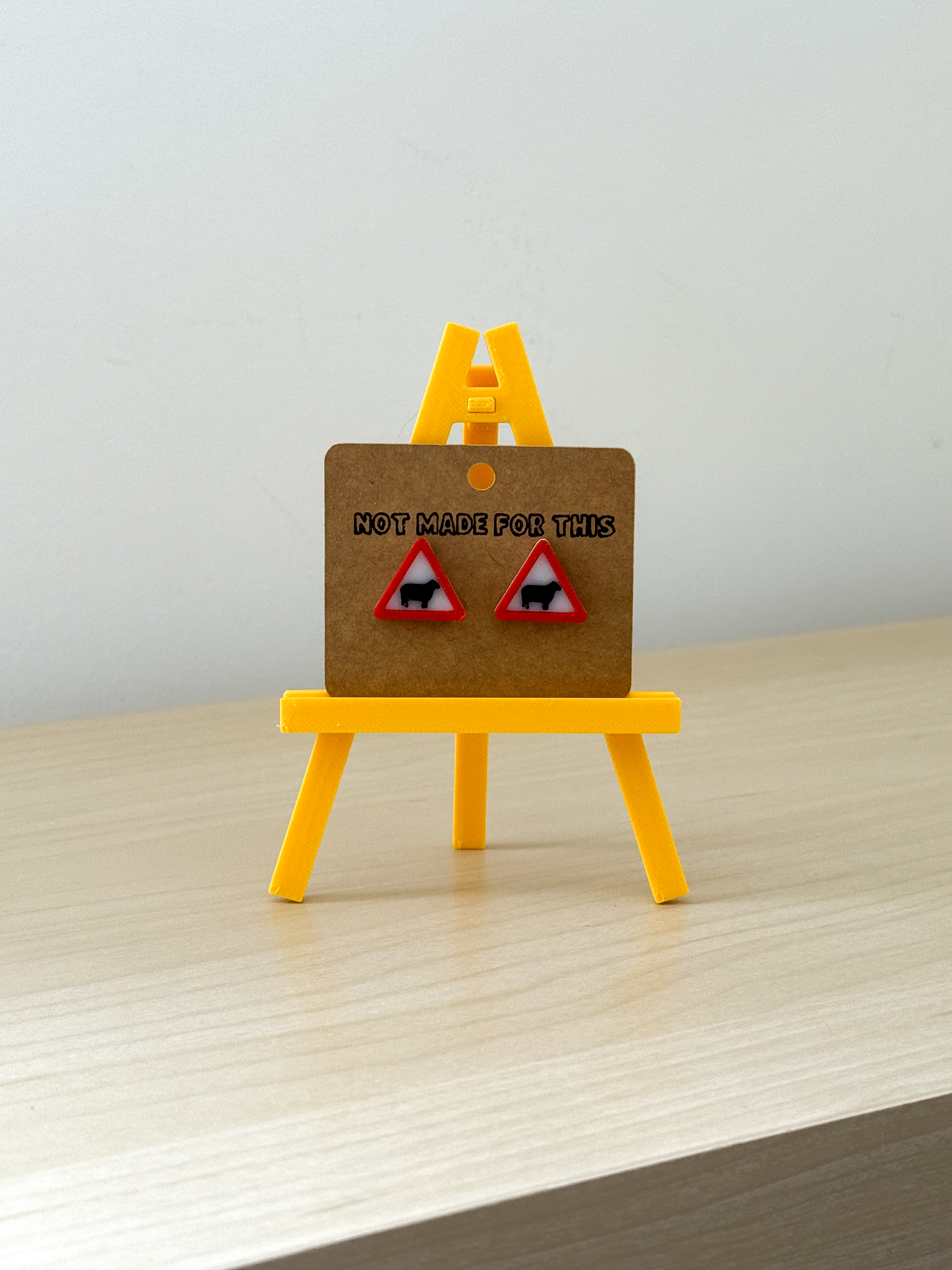 Not Made For This Small wooden board with red triangle warning signs on a yellow stand against a white background