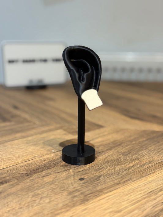 Not Made For This Black ear model on a stand with a white object inside, on a wooden surface.