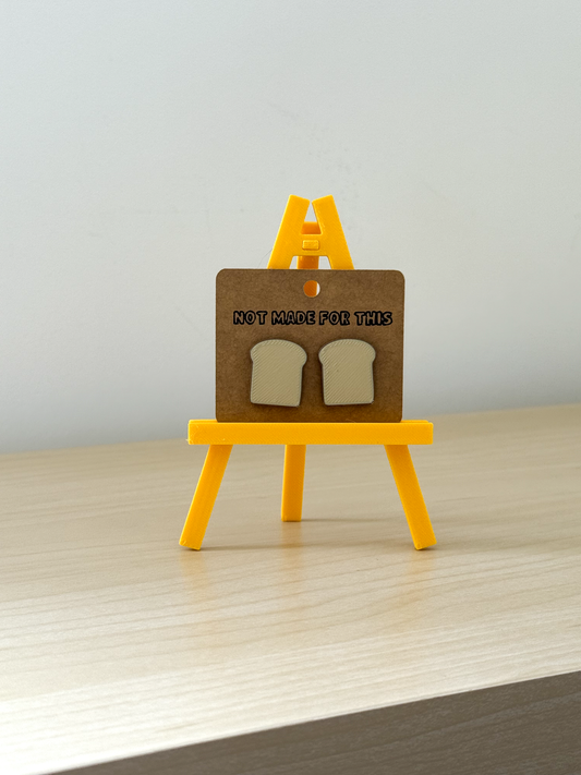 Small wooden easel with bread slices and 'Not Made For This' text on a plain background