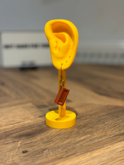 Not Made For This Yellow ear-shaped object with a brown rectangular tag on a wooden surface