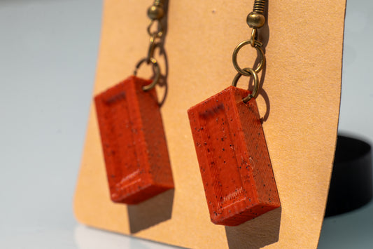 Red rectangular earrings on a beige display card with a blurred background