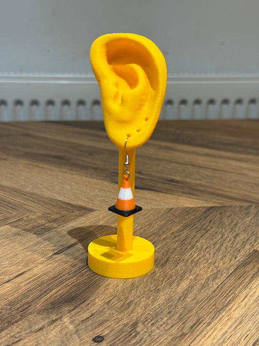 Yellow ear-shaped object with a Not Made For This traffic cone earring on a wooden surface