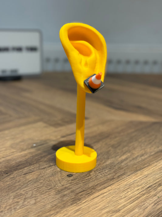 Yellow ear-shaped stand with a small cone earring by Not Made For This on a wooden surface