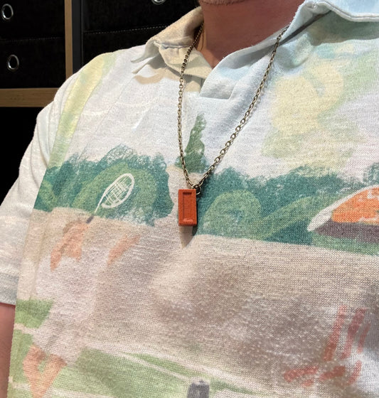 Person wearing a necklace with a rectangular pendant, standing in front of a blurred background.