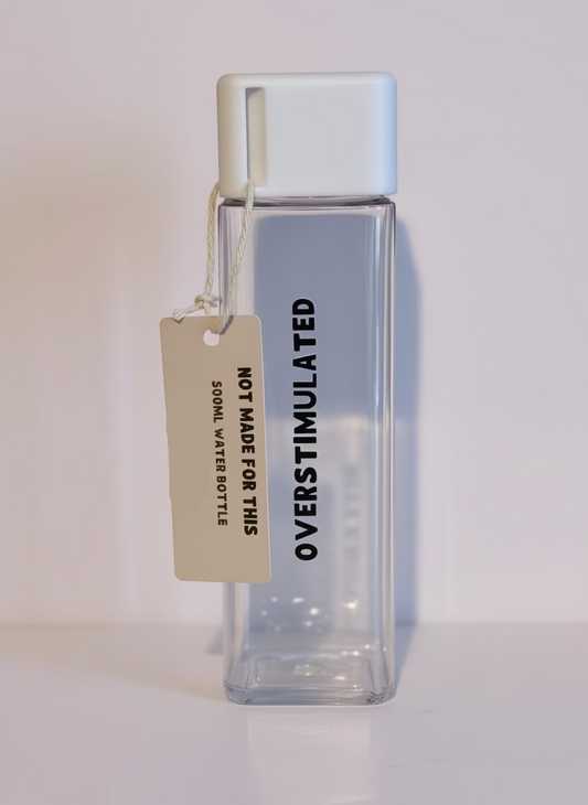 Clear water bottle with a tag labeled 'Not Made for This Overstimulated' on a wooden surface. 
