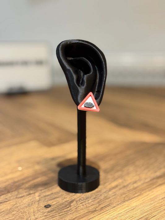 Black 3D-printed ear model with a red and white triangle on a wooden surface made by Not Made For This