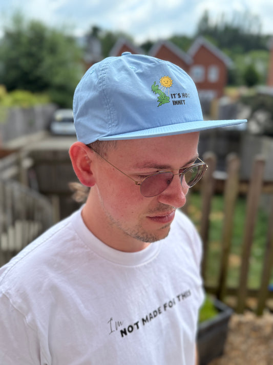 Person wearing a light blue cap and white t-shirt with text outdoors Not Made For This shirt