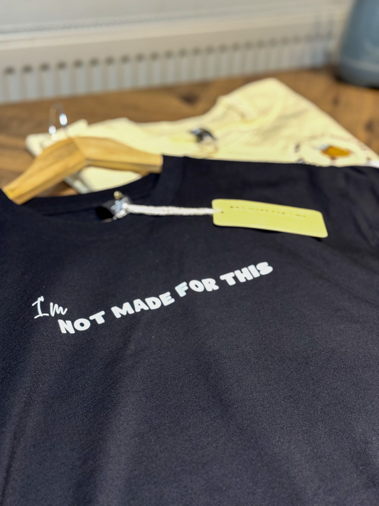 Black shirt with text 'I'm Not Made For This' on a wooden surface.
