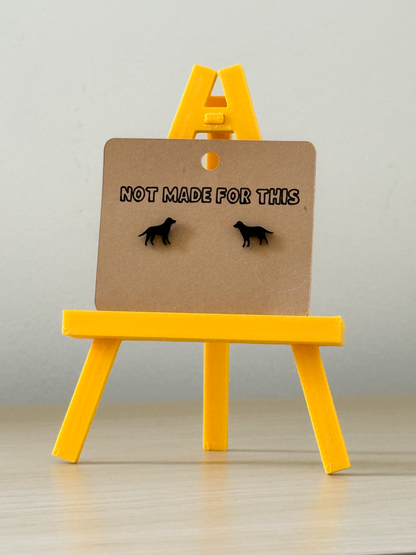 Pair of earrings on a card with 'Not Made For This' text on a yellow stand against a gray background.