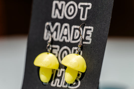 Yellow mushroom-shaped earrings on a black card with Not Made For This