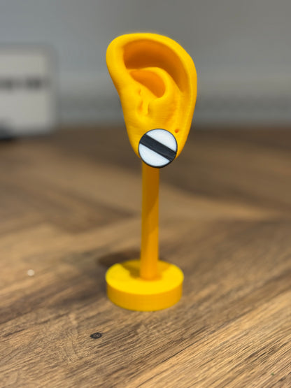 Not Made For This Yellow ear-shaped object with a black and white circle on a wooden surface