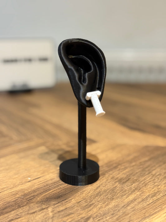 Black ear-shaped jewelry stand with a Not Made For This pillar earring on a wooden surface