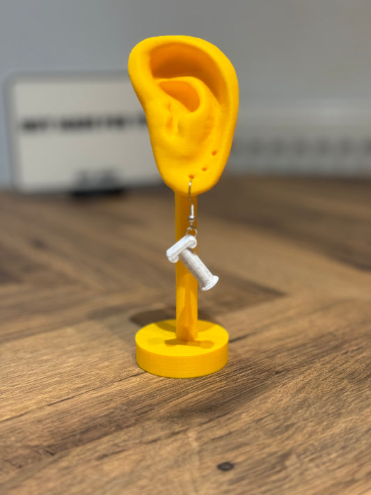 Yellow ear-shaped stand with a white Not Made For This  pillar earring on a wooden surface