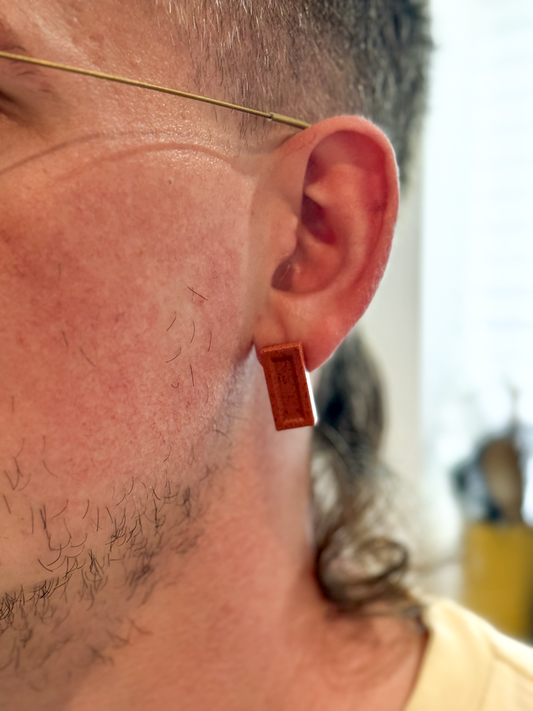 Close-up of a person's ear with a small brick earring. His hair is awesome.