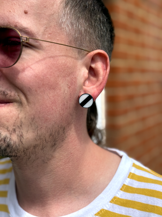 Close-up of a person wearing black and white striped earrings with a blurred brick wall background.