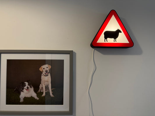 Framed picture of two dogs on a wall next to a triangular warning sign with a sheep silhouette made by Not Made For This