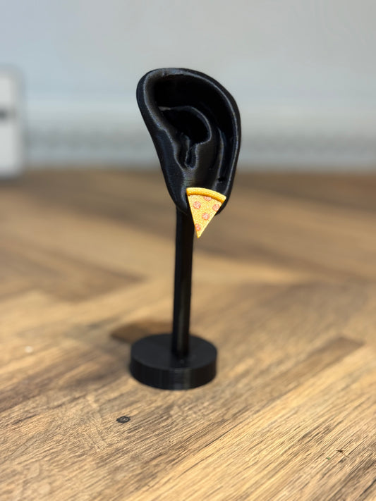 Black ear-shaped stand with a small pizza slice on a wooden surface