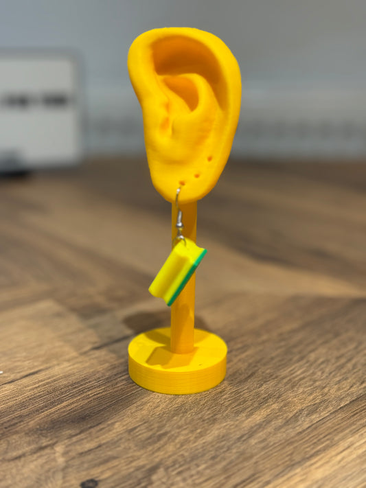Not Made For This Yellow ear-shaped stand with earrings on a wooden surface