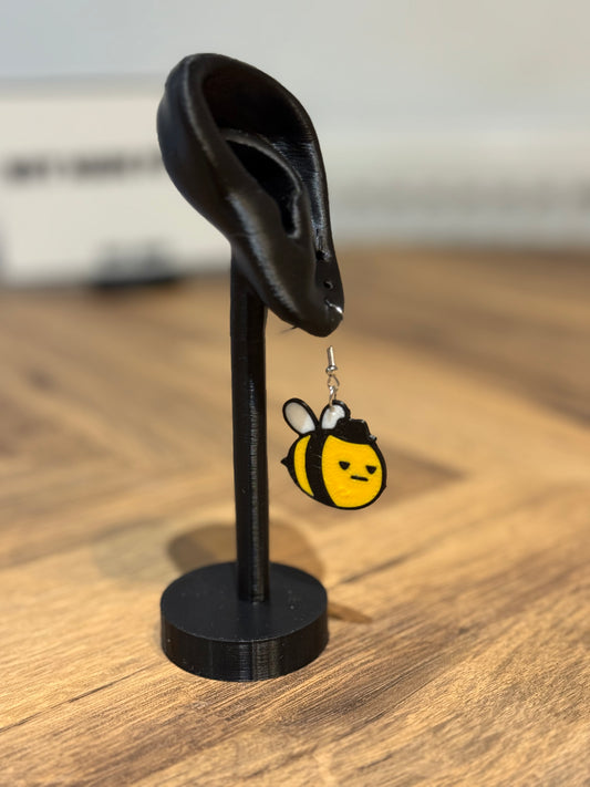 Not Made For This Bee-shaped earring on a black stand with a blurred background